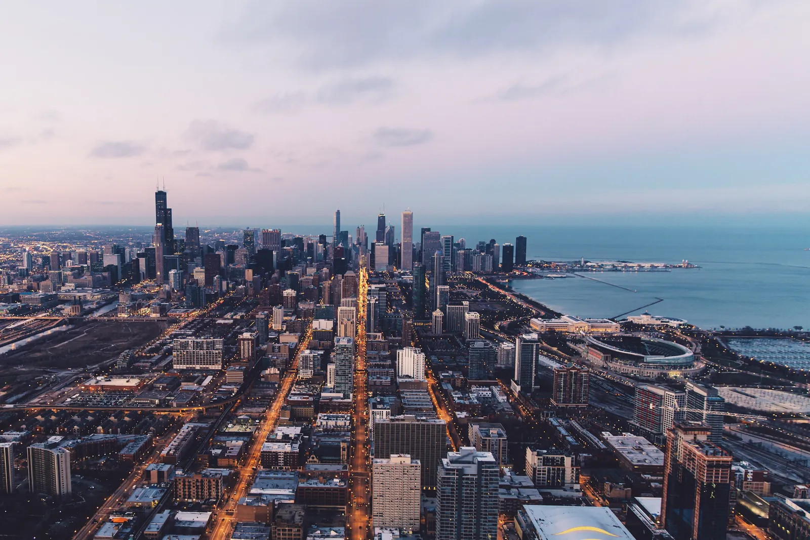 Aerial view of the Chicago skyline at dusk with lit streets and Lake Michigan beyond