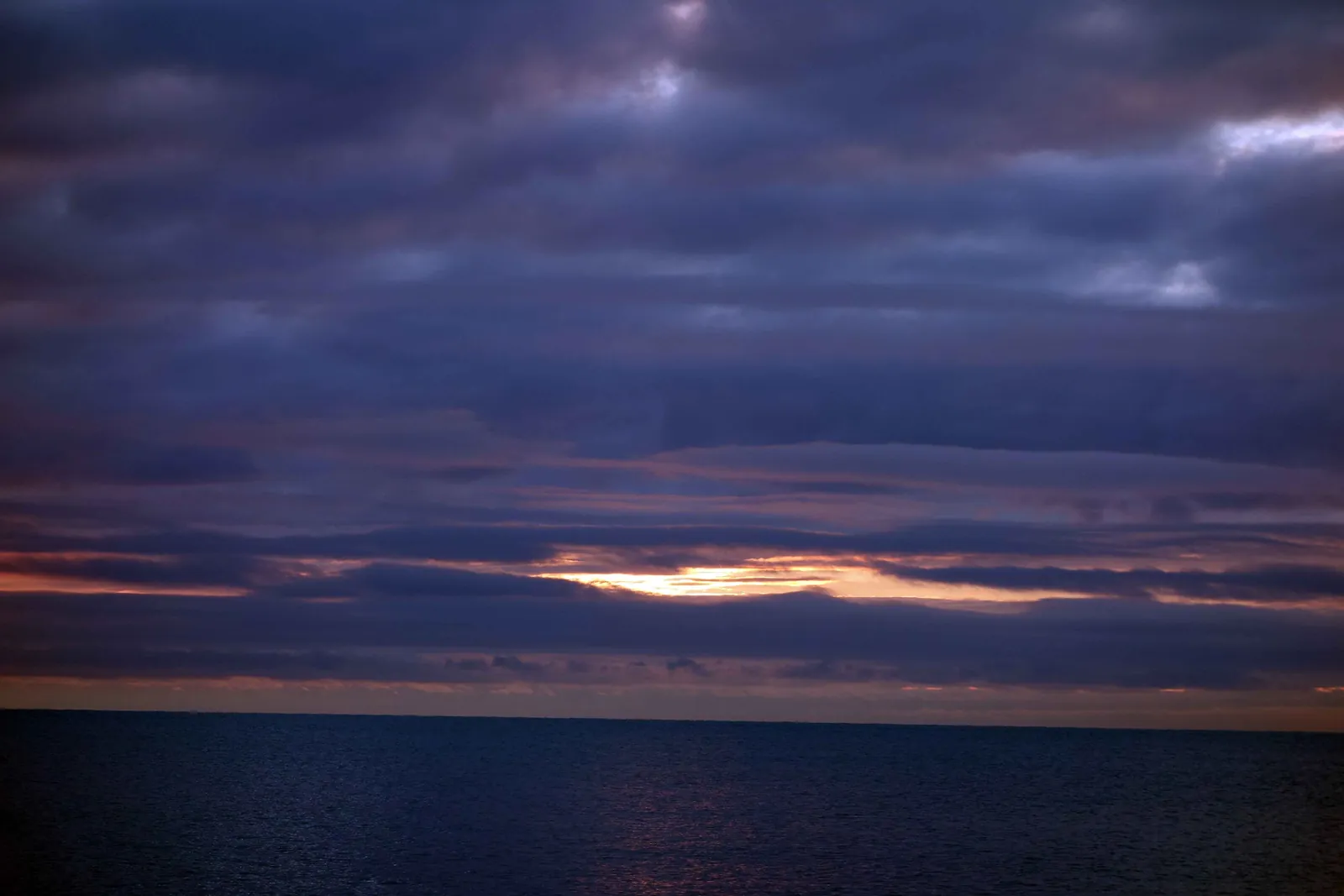 A thin band of orange dawn light under heavy grey clouds above dark lake water