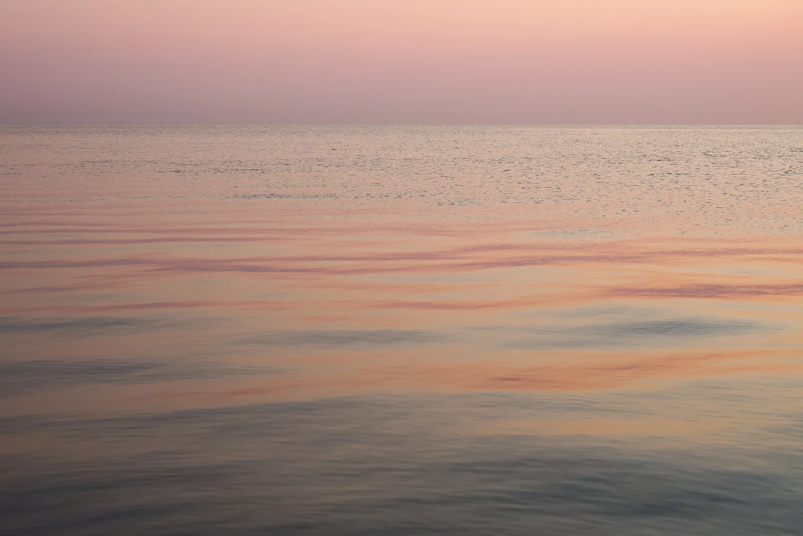 Calm, faintly rippled water under a soft pink and lavender sky, with pastel light reflected across the lake